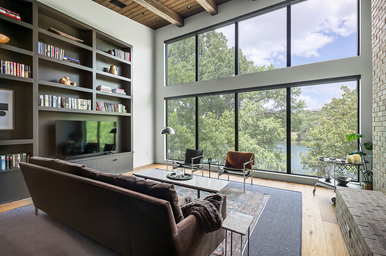 Living room with white oak floors, a brick column and framed Lake Austin views, furnished by Liz MacPhail Interiors at 2403 Big Horn Drive, Austin.