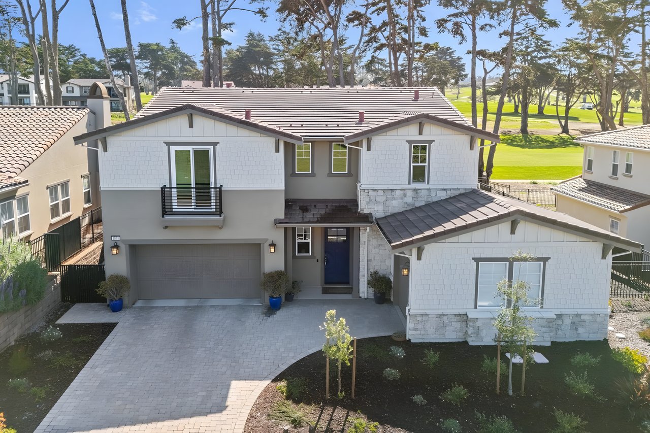 Two-story gray and white home with stone accents, a blue front door, and golf course behind it.