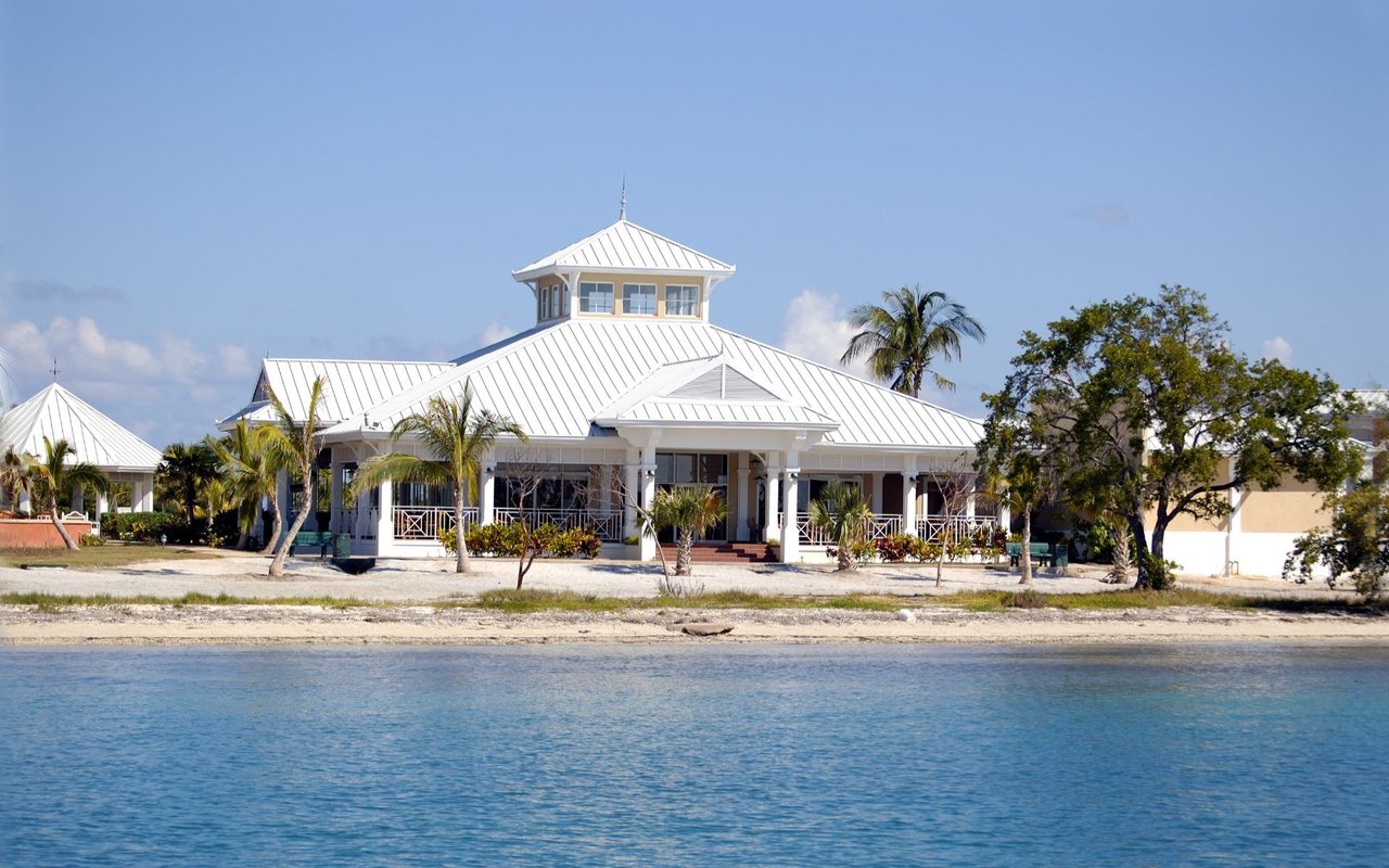White waterfront pavilion with a cupola and palm trees beside blue water.