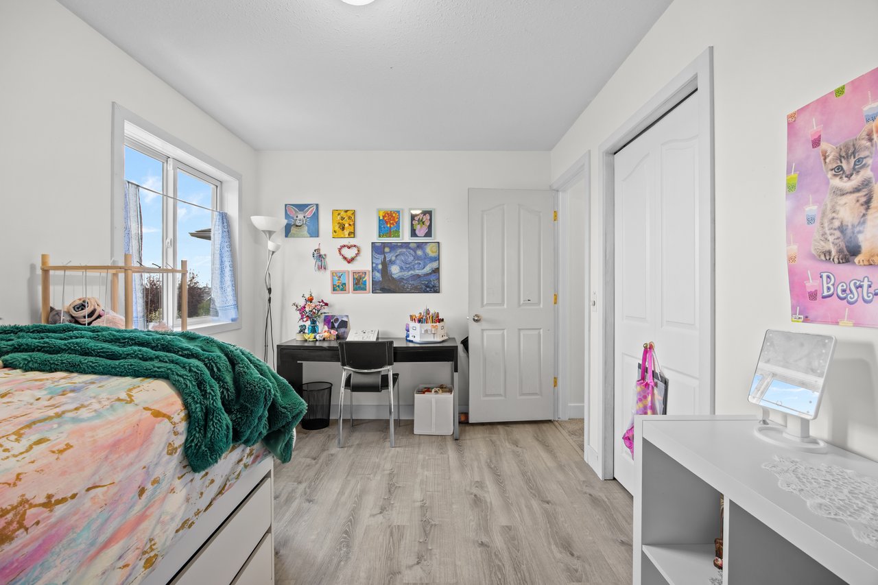 Bedroom with a colorful bed, deep teal blanket, desk, and bright window.