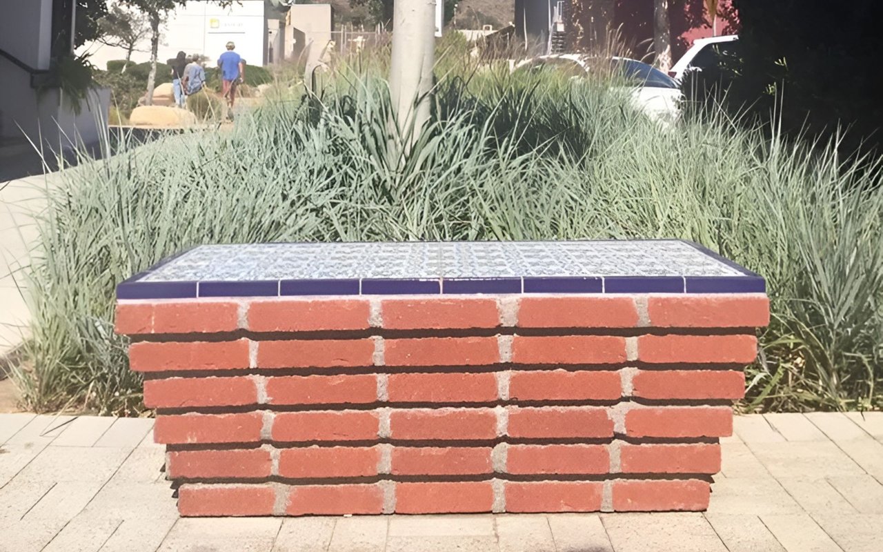 Brick bench with a tiled seat amid ornamental grasses at an outdoor shopping center.