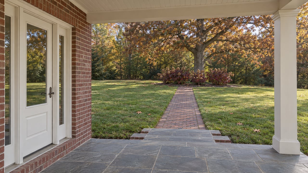 Covered brick entry with slate steps and a brick walk opening onto a broad autumn lawn beneath a mature oak.