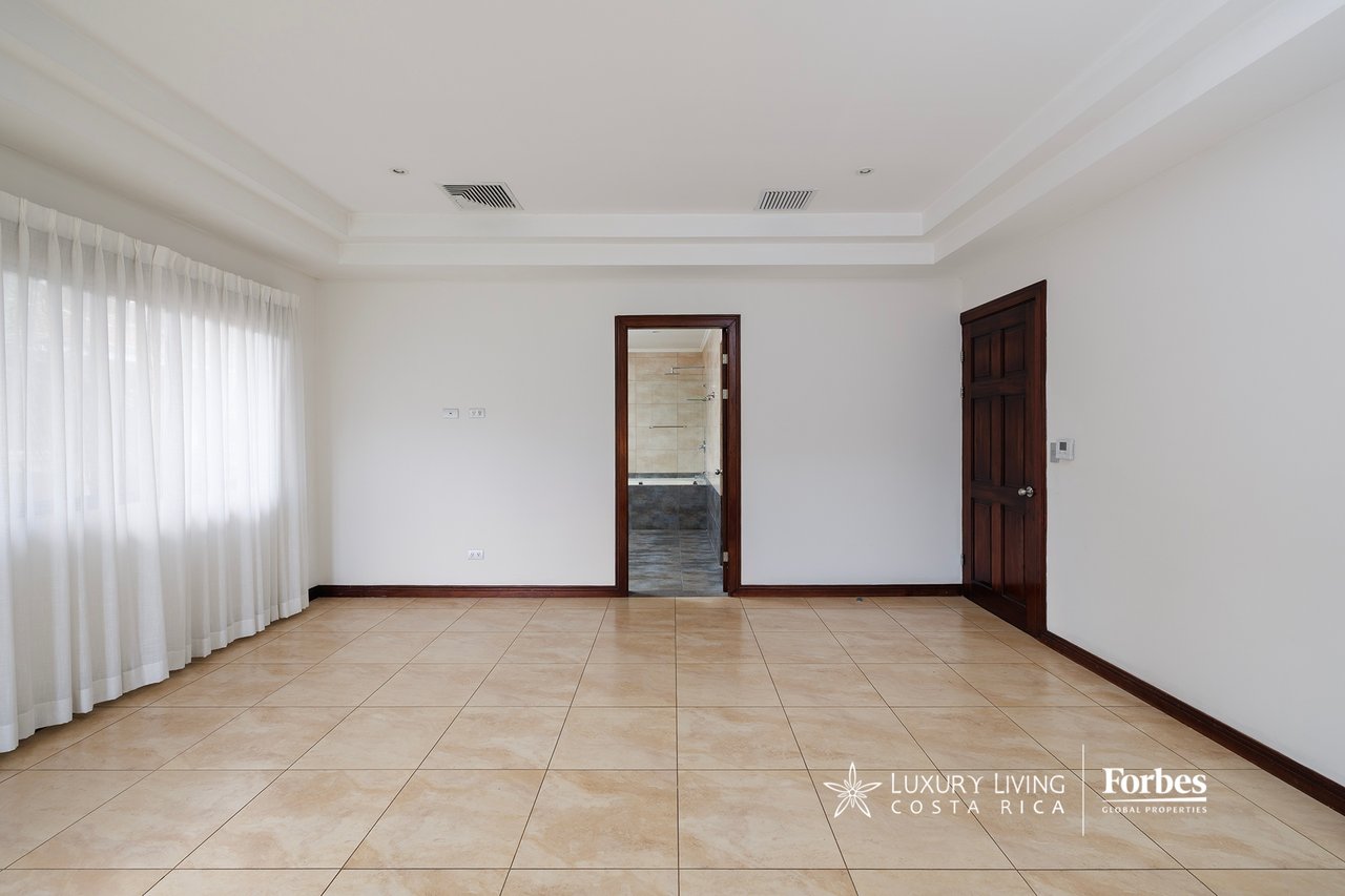 Empty tiled room with sheer curtains and a bathroom visible through the doorway.