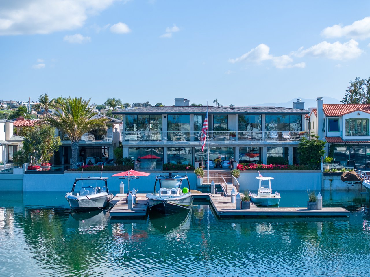 Modern waterfront home with floor-to-ceiling windows, a dock, and boats on the canal.
