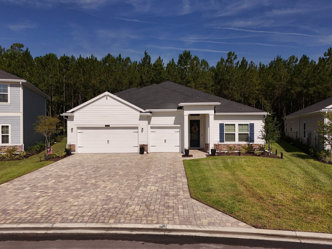 White single-story home with blue shutters, a two-car garage, and a wide paver driveway.