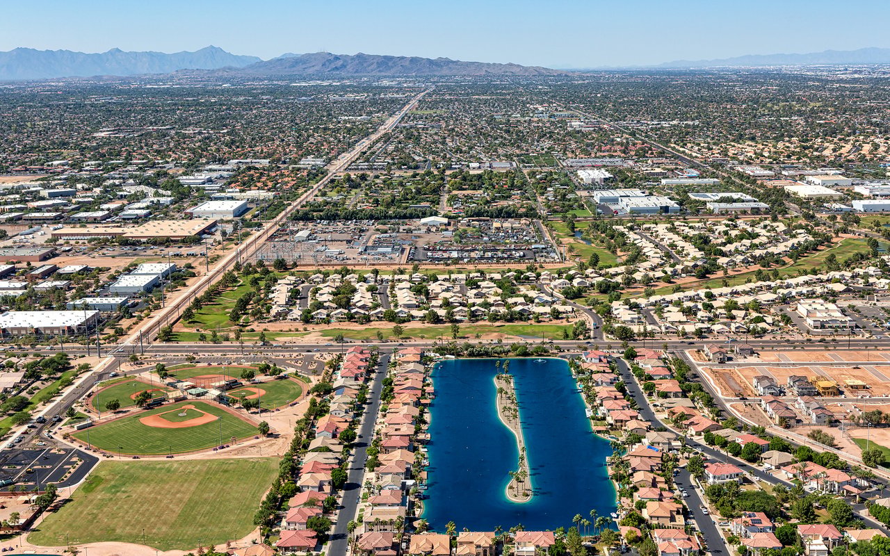 Aerial view of a residential neighborhood with a central lagoon, baseball fields, and distant mountains.