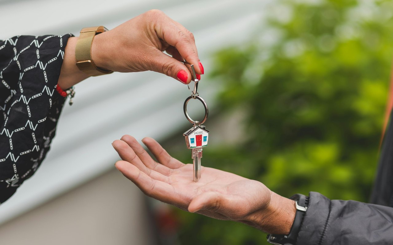 A house key with a “HOME” keychain is handed from one person to another.