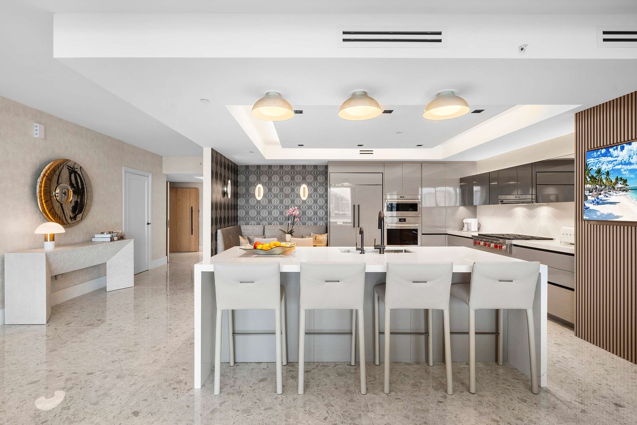 Sleek kitchen with island, white countertops, bench seating, geometric wallpaper, large fridge, and high-end built-in appliances.