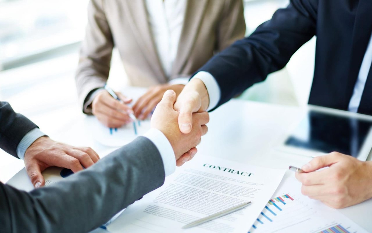 A cordial partnership is sealed as businessmen exchange documents and shake hands.