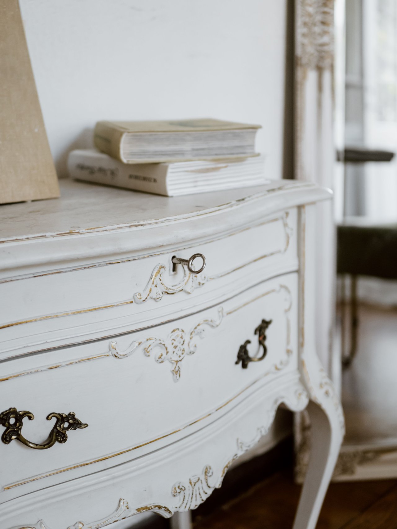 Ornate white antique dresser with brass hardware and stacked books.