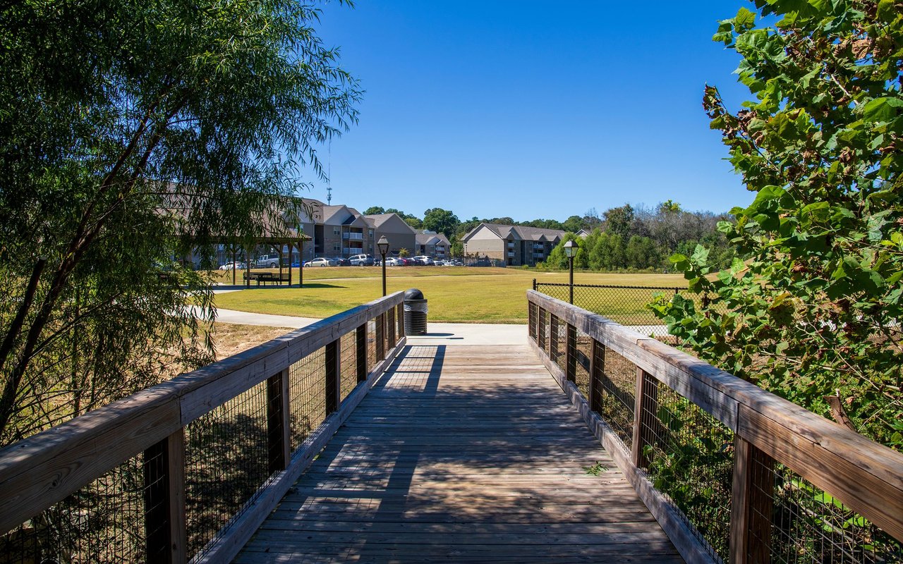 Wooden bridge crosses a neighborhood park toward apartment buildings.