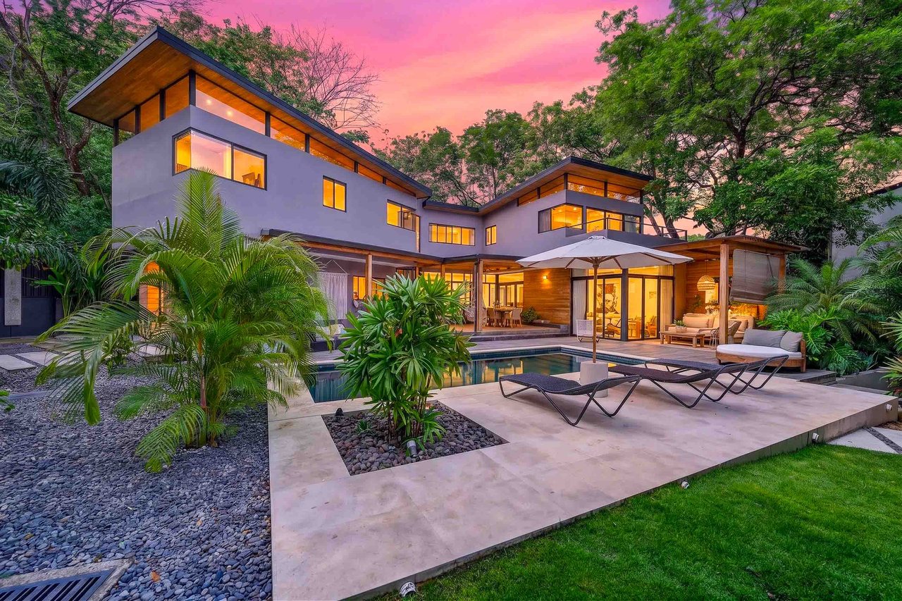 Modern home with a pool and furnished patio surrounded by tropical plants at dusk.