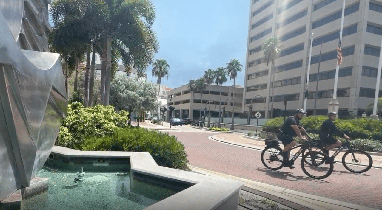 Downtown Sarasota roundabout with a fountain, palm trees, and two cyclists.