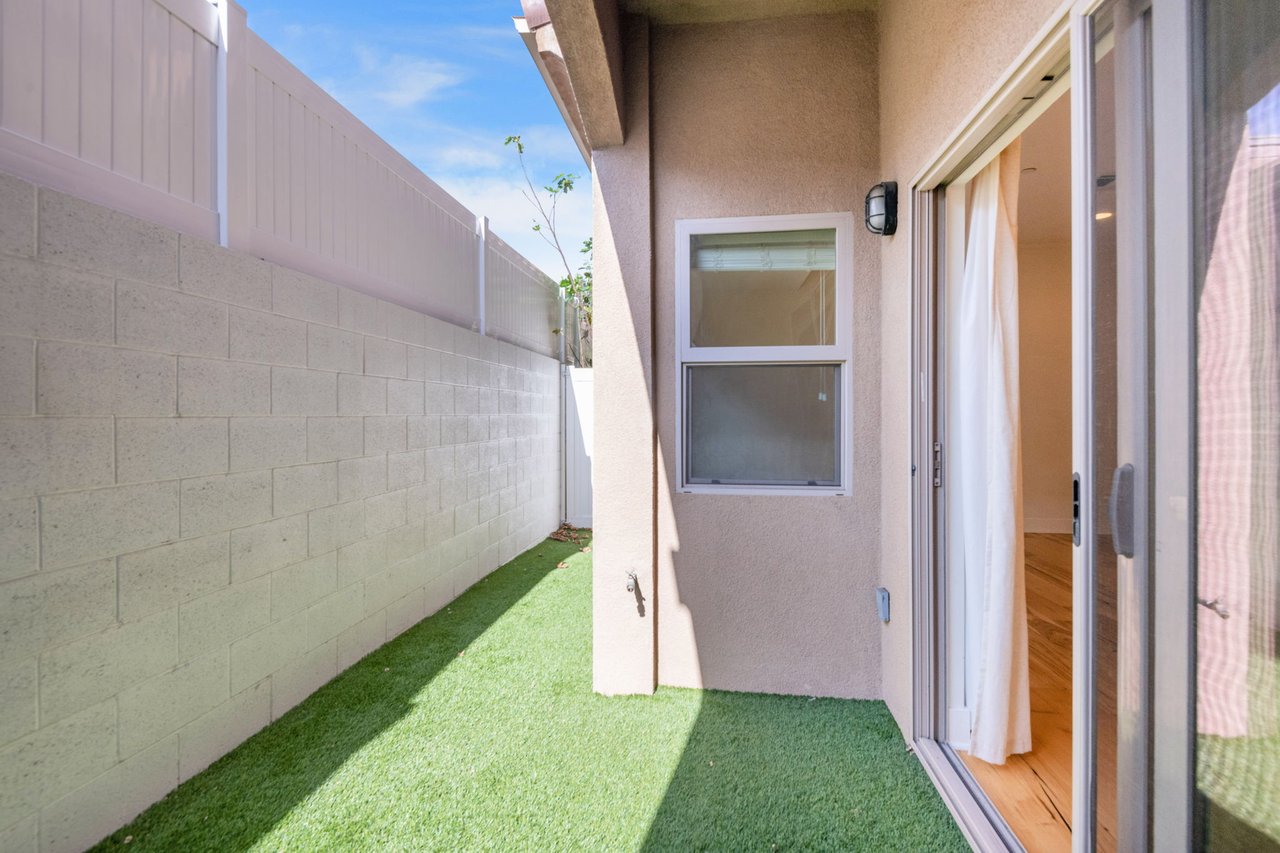 Private side patio with artificial turf, block privacy wall, and exterior entry door