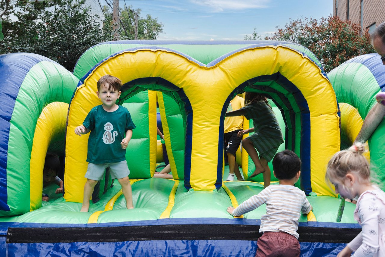 Children play on a green-and-yellow inflatable obstacle course outdoors.