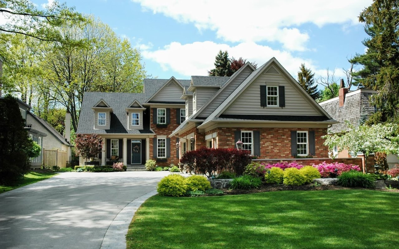 A traditional multi-gabled family residence displaying exceptional curb appeal, custom brickwork, multiple dormers, a front porch, and lush professional garden landscaping.