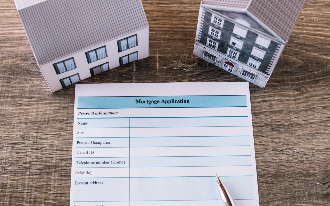 Mortgage application form beside two model houses and a pen on a wooden table.