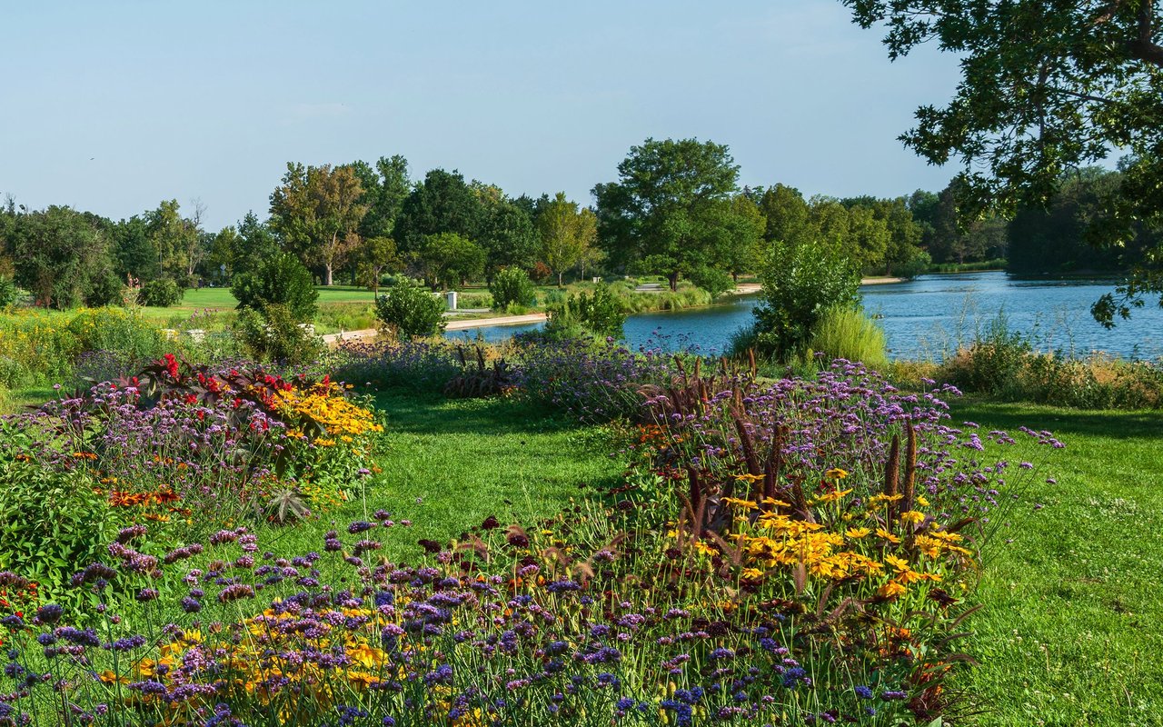 Washington Park with colorful flower beds, green lawn, mature trees, and a lake.