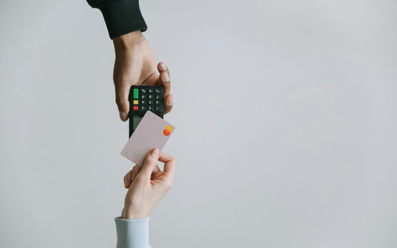 Hands holding a payment card and card terminal against a plain background.