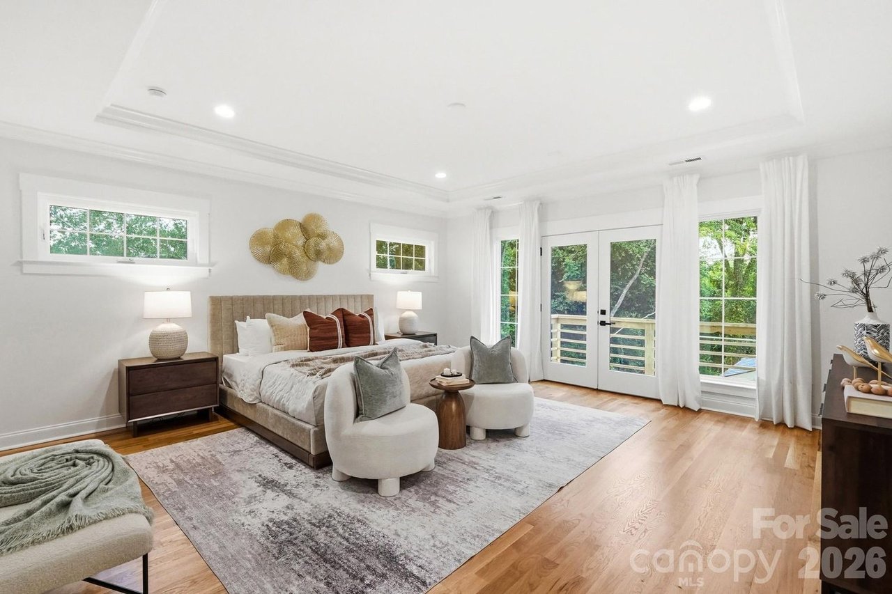 Bright staged bedroom with a king bed and French doors opening onto a leafy deck.
