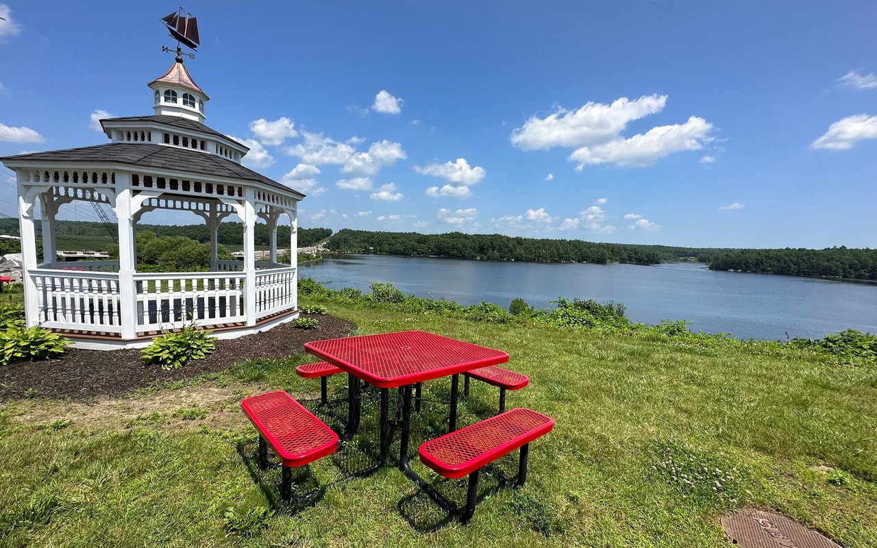 White gazebo and red picnic table beside a broad river in Woolwich.