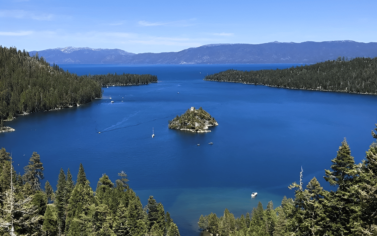 Lake Tahoe’s blue water and forested shores, with a small rocky island and mountains beyond.