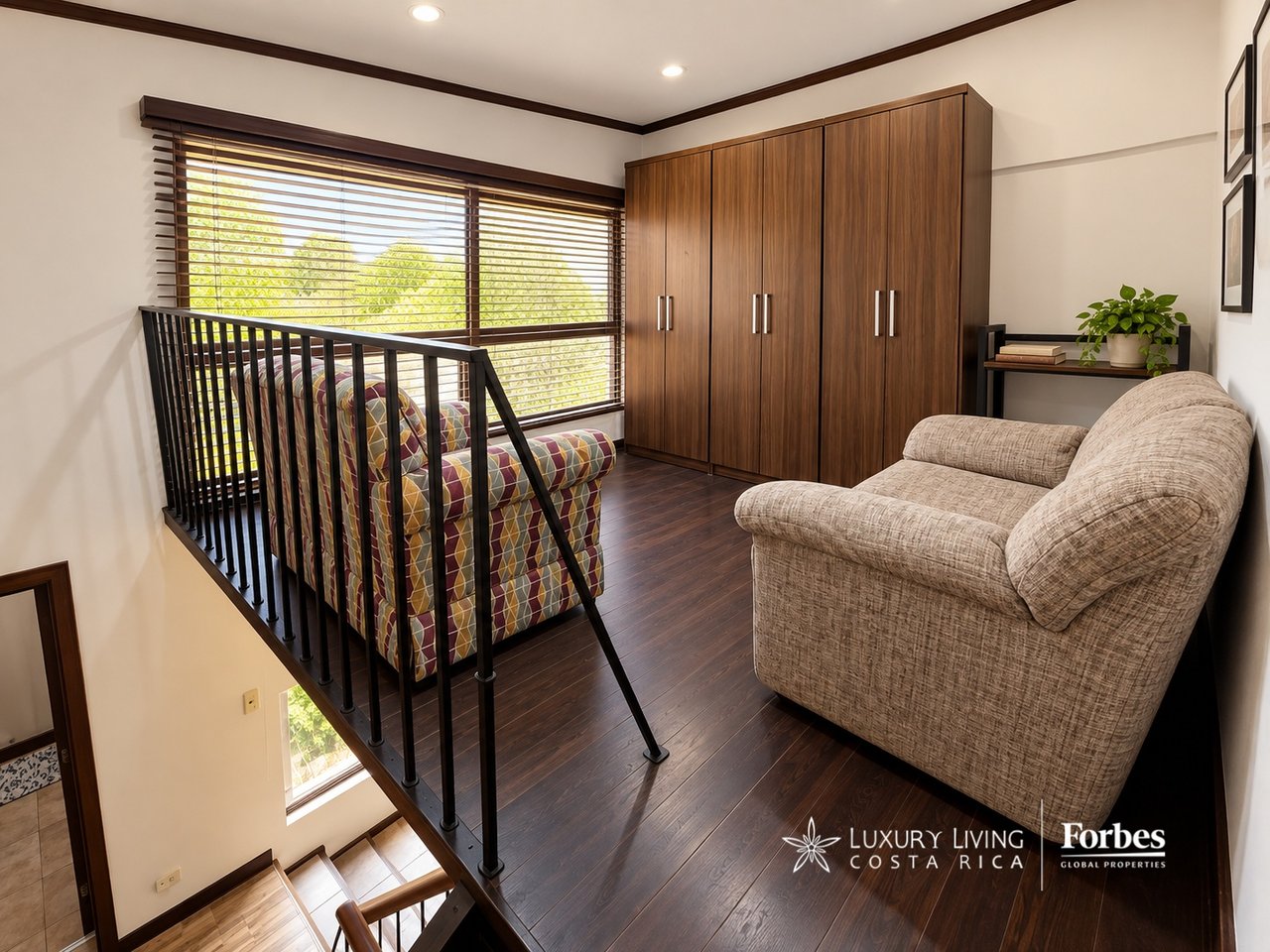 Furnished loft sitting area with patterned sofa, beige armchair, and wide windows overlooking greenery.