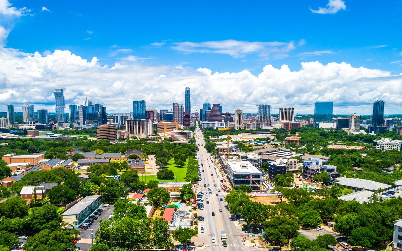Aerial view of downtown Austin with a tree-lined road leading toward the skyline.