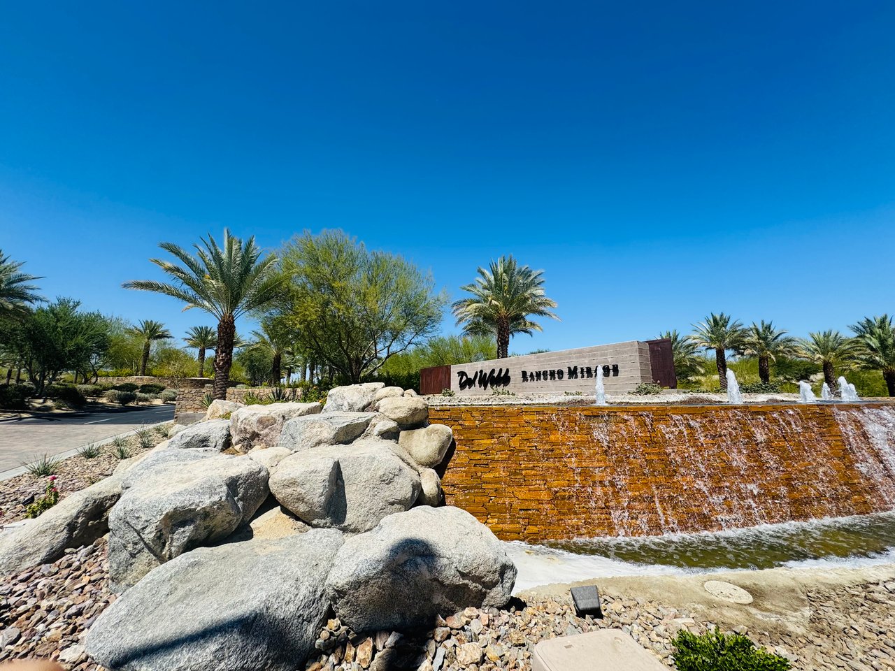 The Dunes at Rancho Mirage entrance sign above a stone waterfall fountain and desert landscaping.