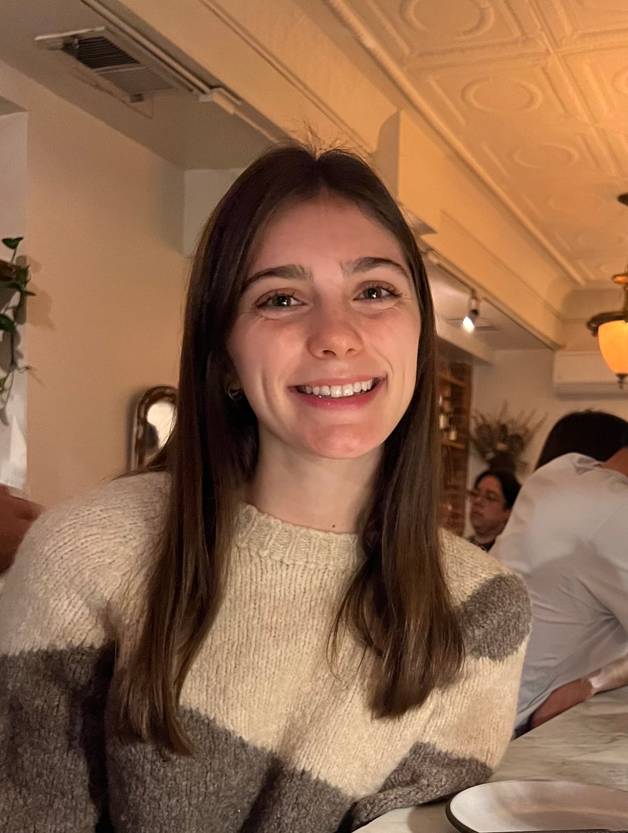 Smiling woman with long dark hair wearing a cream and gray knit sweater.