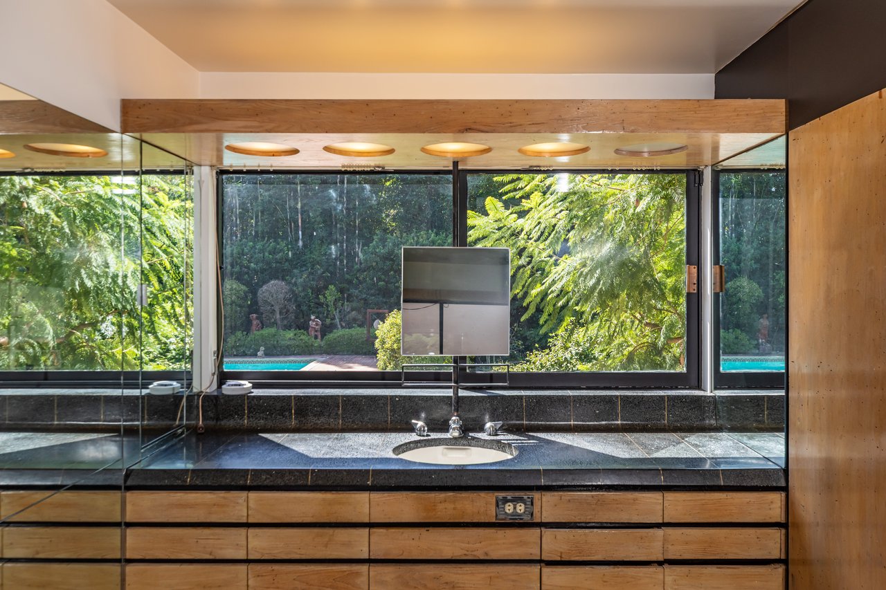 Bathroom vanity with wood cabinetry and a window overlooking the pool and garden.