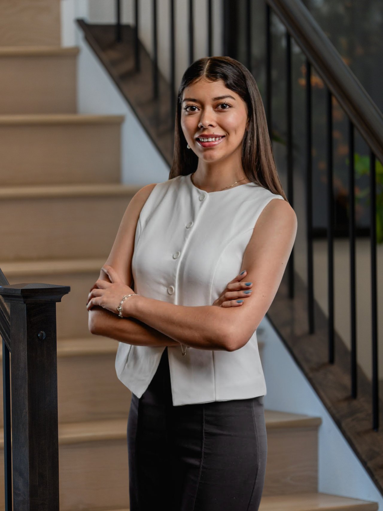 Diana Reyes poses with crossed arms beside a staircase, wearing a white sleeveless vest.