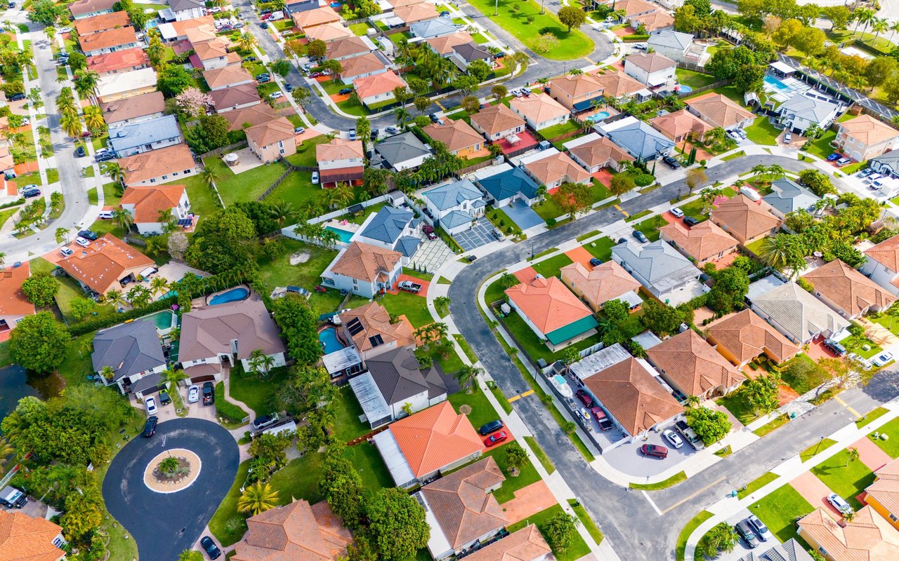 West Miami homes and tree-lined streets viewed from above, with a curved road and backyard pools.