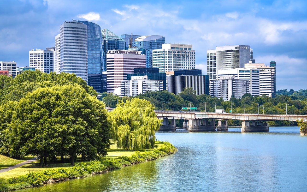 City skyline across a river, with a bridge and leafy waterfront in the foreground.
