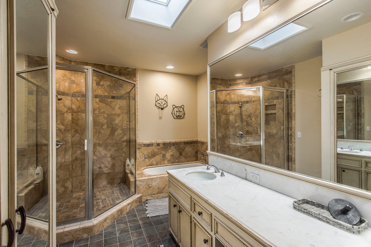 Bathroom with dual glass showers, a soaking tub, marble vanity, and skylights.