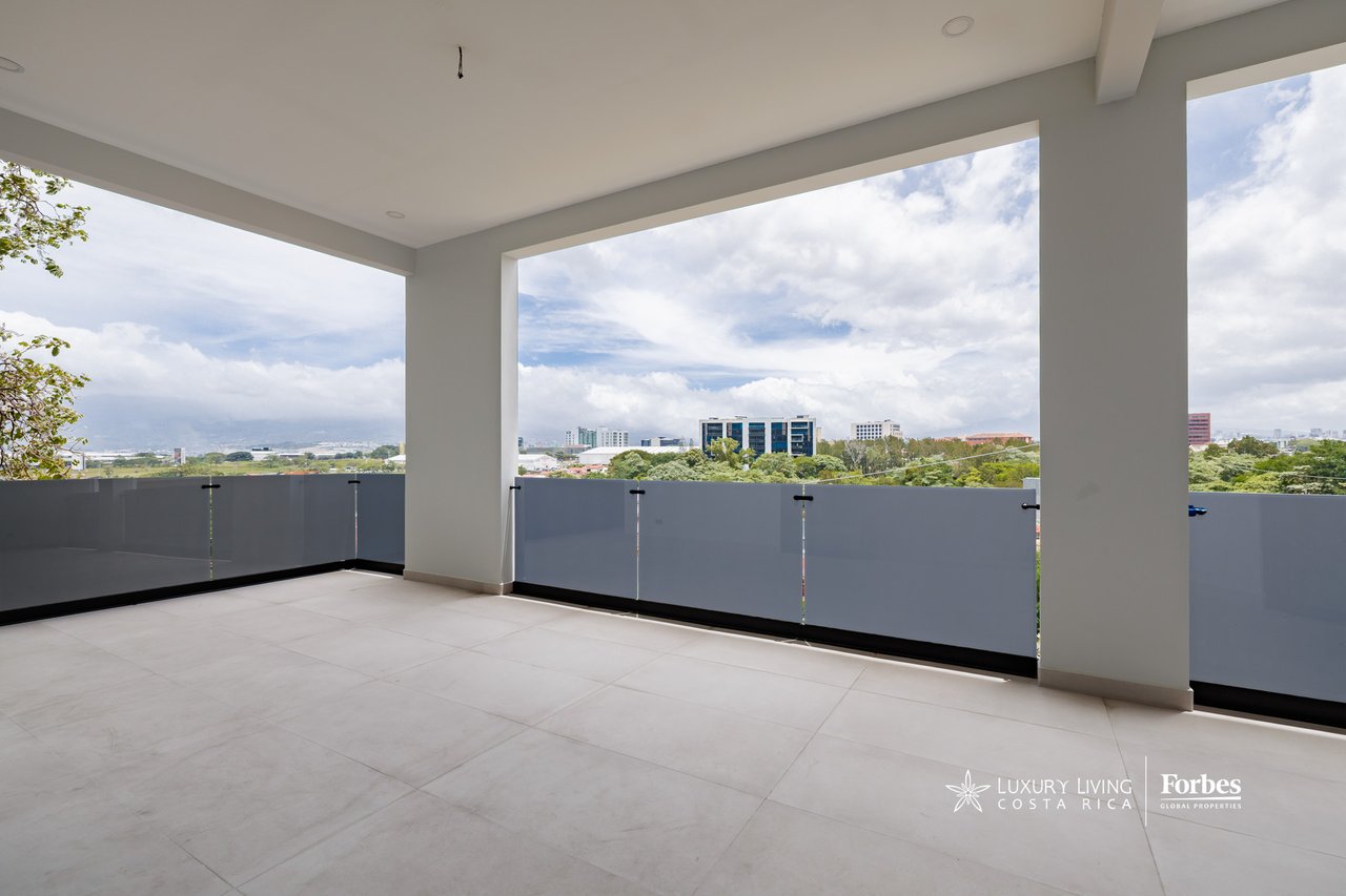 Covered apartment balcony with tiled floor and treetop and city views.