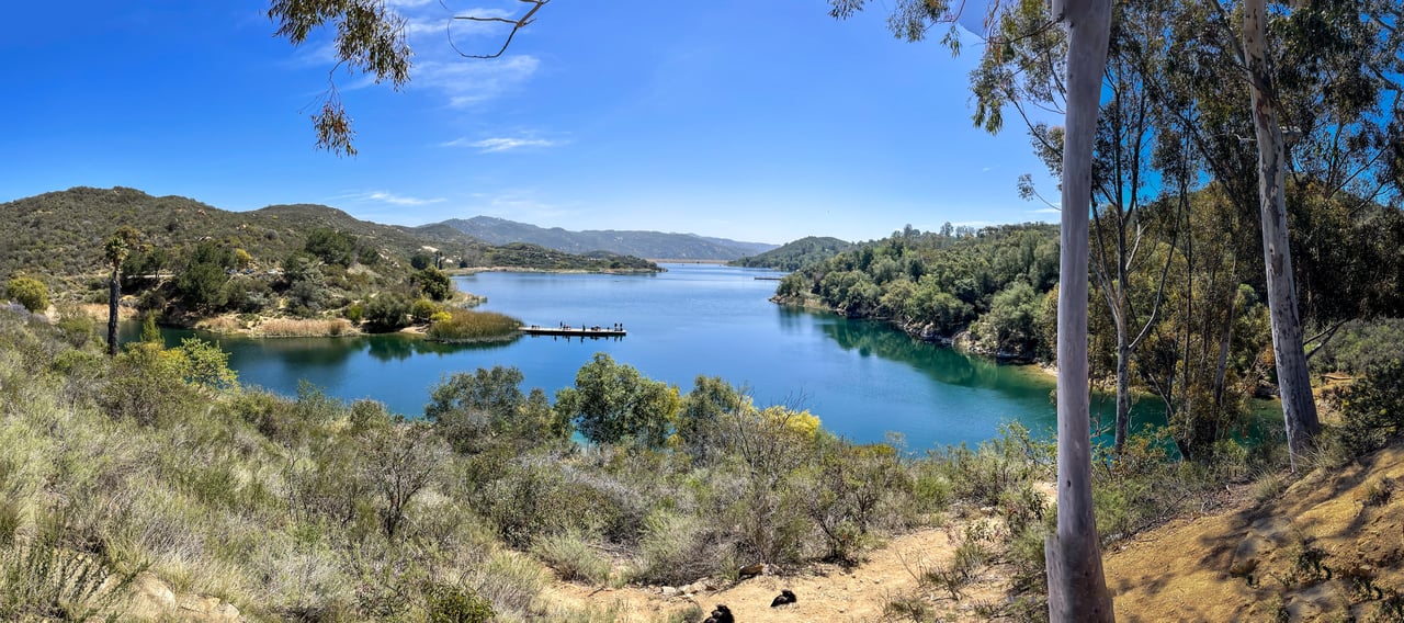 Lake surrounded by green hills, with a small dock extending into the water.