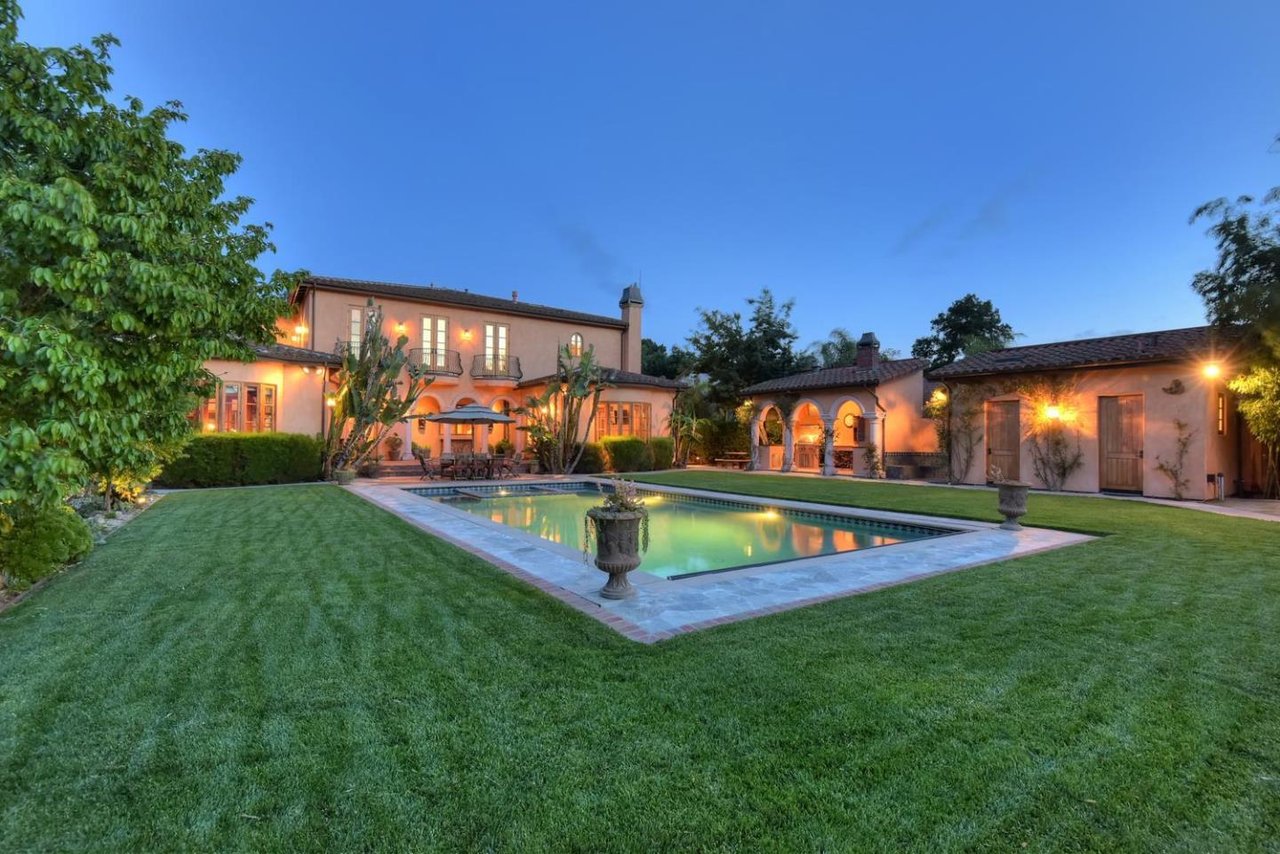 Mediterranean-style home with a lit courtyard and swimming pool at dusk