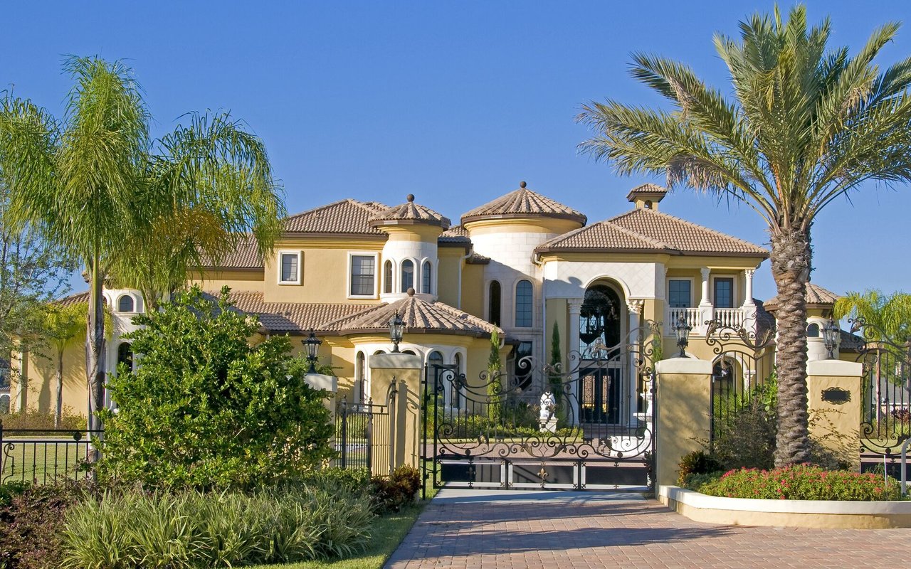 Mediterranean-style home behind ornate wrought-iron gates, framed by palm trees.