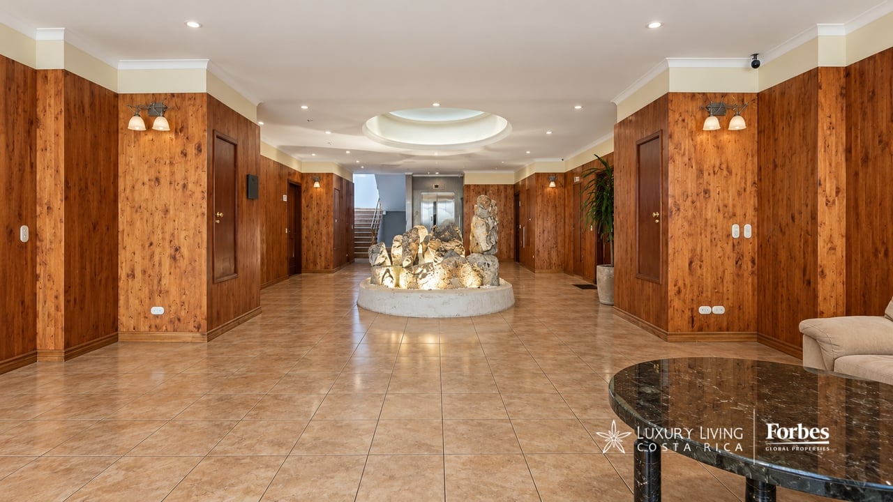 Wood-paneled building lobby with an illuminated stone sculpture display, elevator, and staircase.