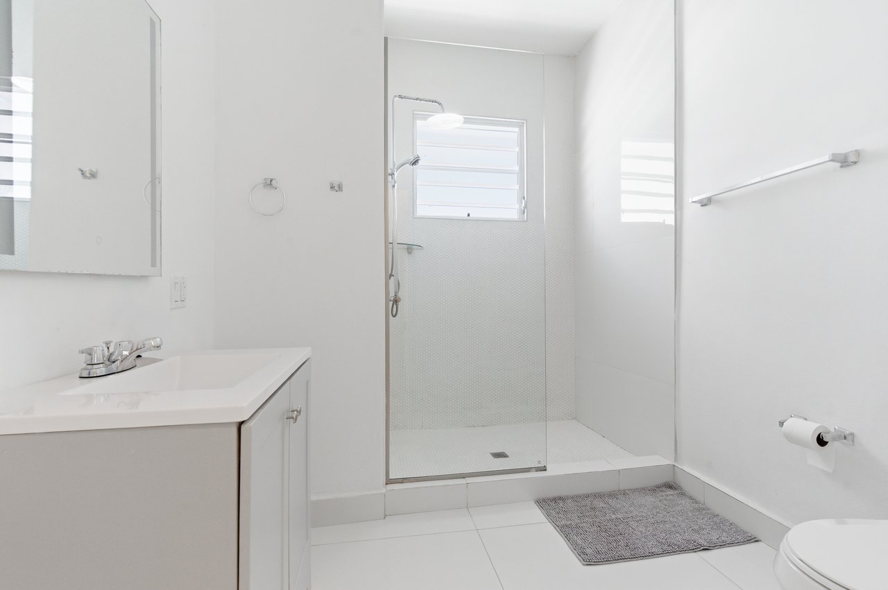 White bathroom with a glass-enclosed walk-in shower and single-sink vanity.