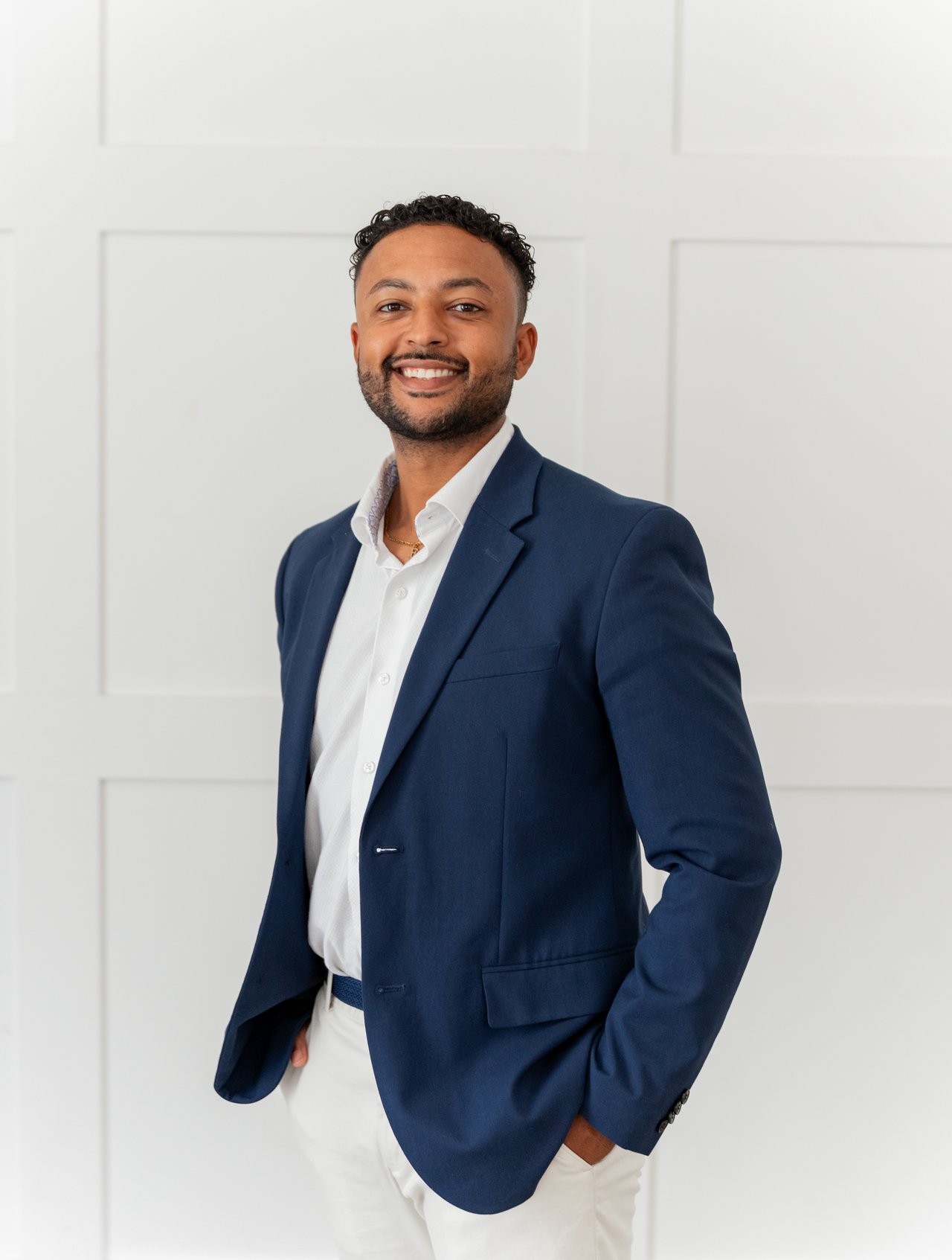 Brandon Allen in a navy suit and white shirt, smiling against a white paneled wall.