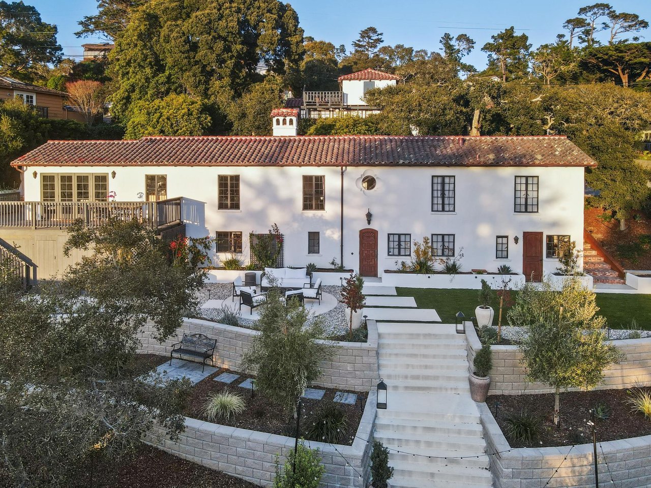 Historic white Spanish-style home in Carmel-by-the-Sea with terracotta roof, terraced garden, stone steps, and mature trees.