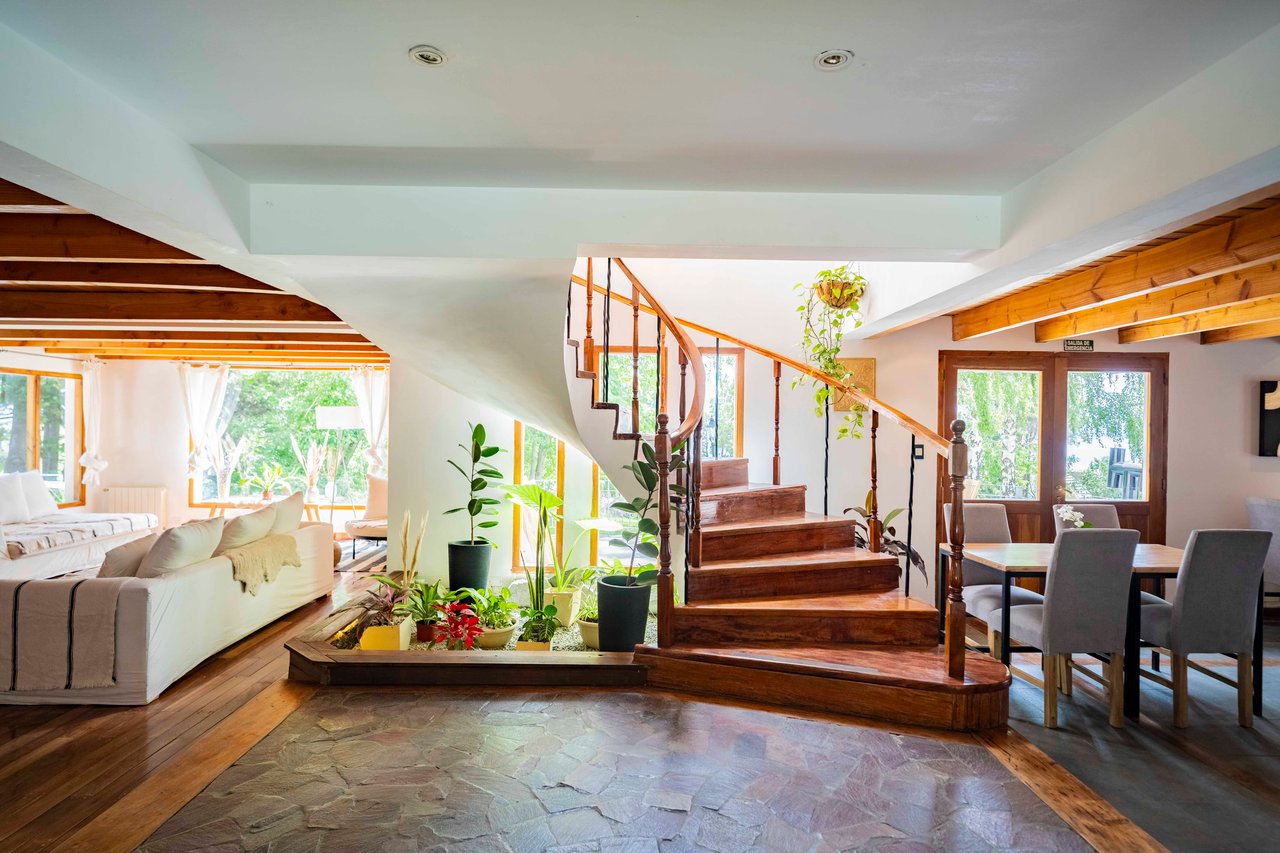 Hotel interior with a curved wooden staircase, timber beams, dining table, and bright living area.