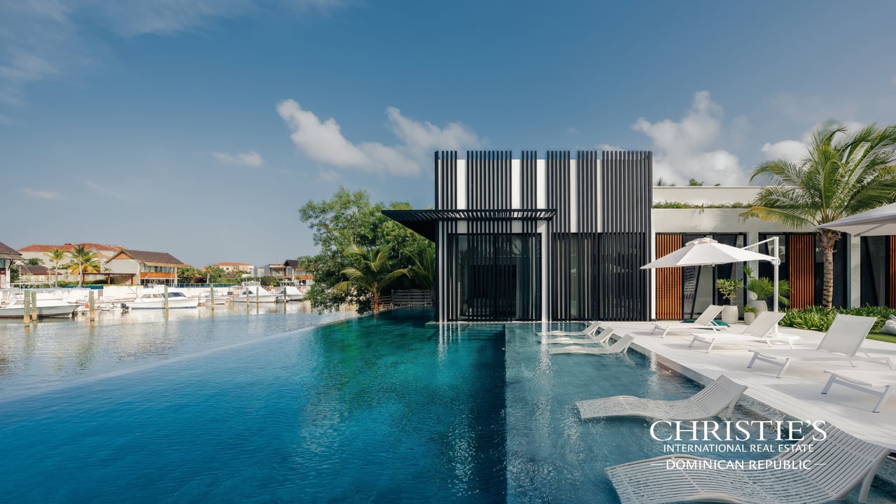 Modern waterfront villa with an infinity pool, poolside loungers, and boats in the marina.
