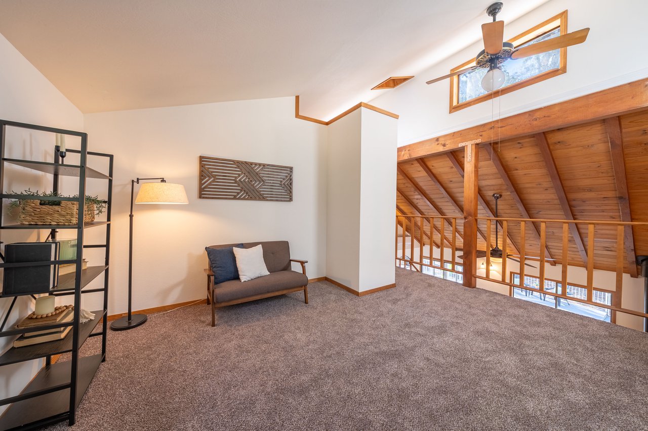 Furnished loft sitting area with a gray loveseat, carpet, and vaulted wood ceiling.