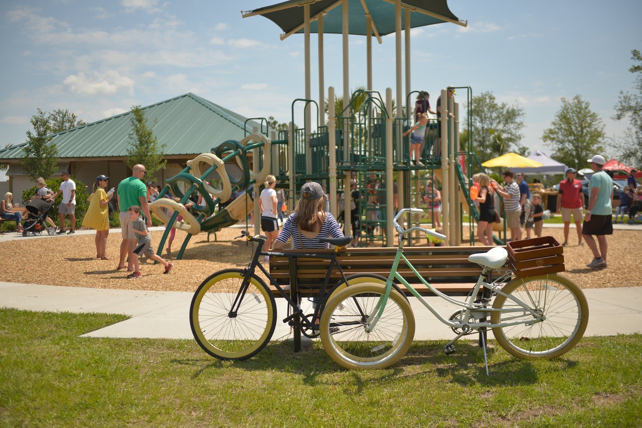 Families gather at a community playground, with bicycles parked beside a bench.