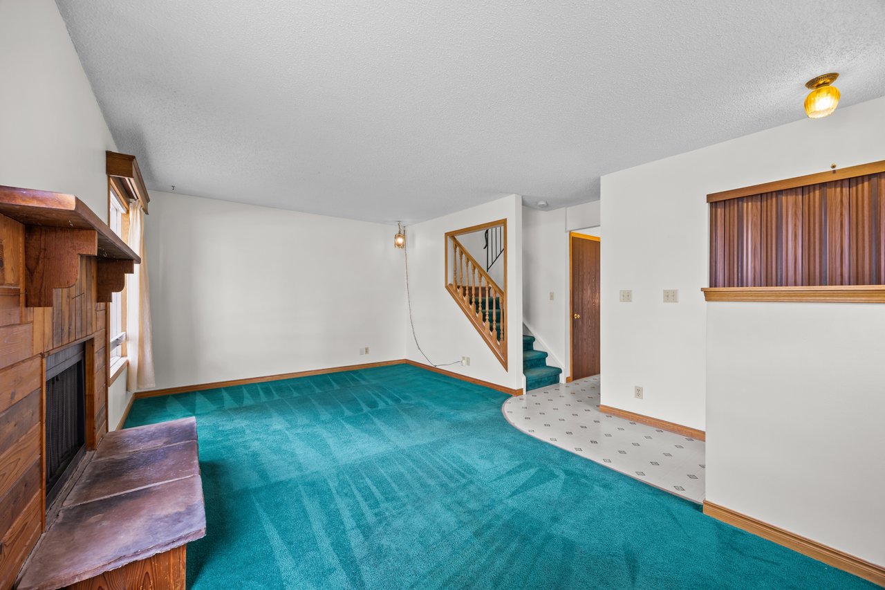 Living room with teal carpeting, a wood-paneled fireplace, and a staircase.