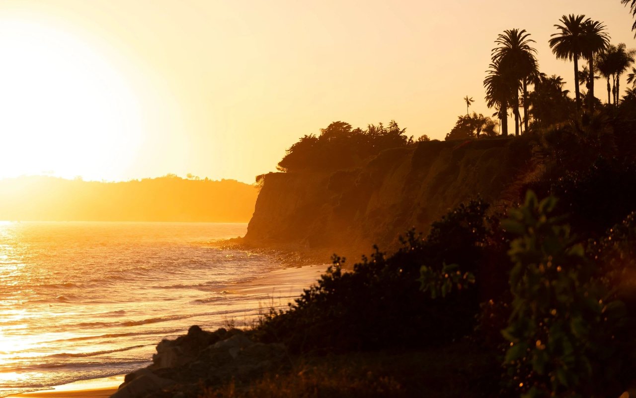 A warm, glowing sunset over a coastline, casting a brilliant orange and yellow hue across the sky and the ocean.
