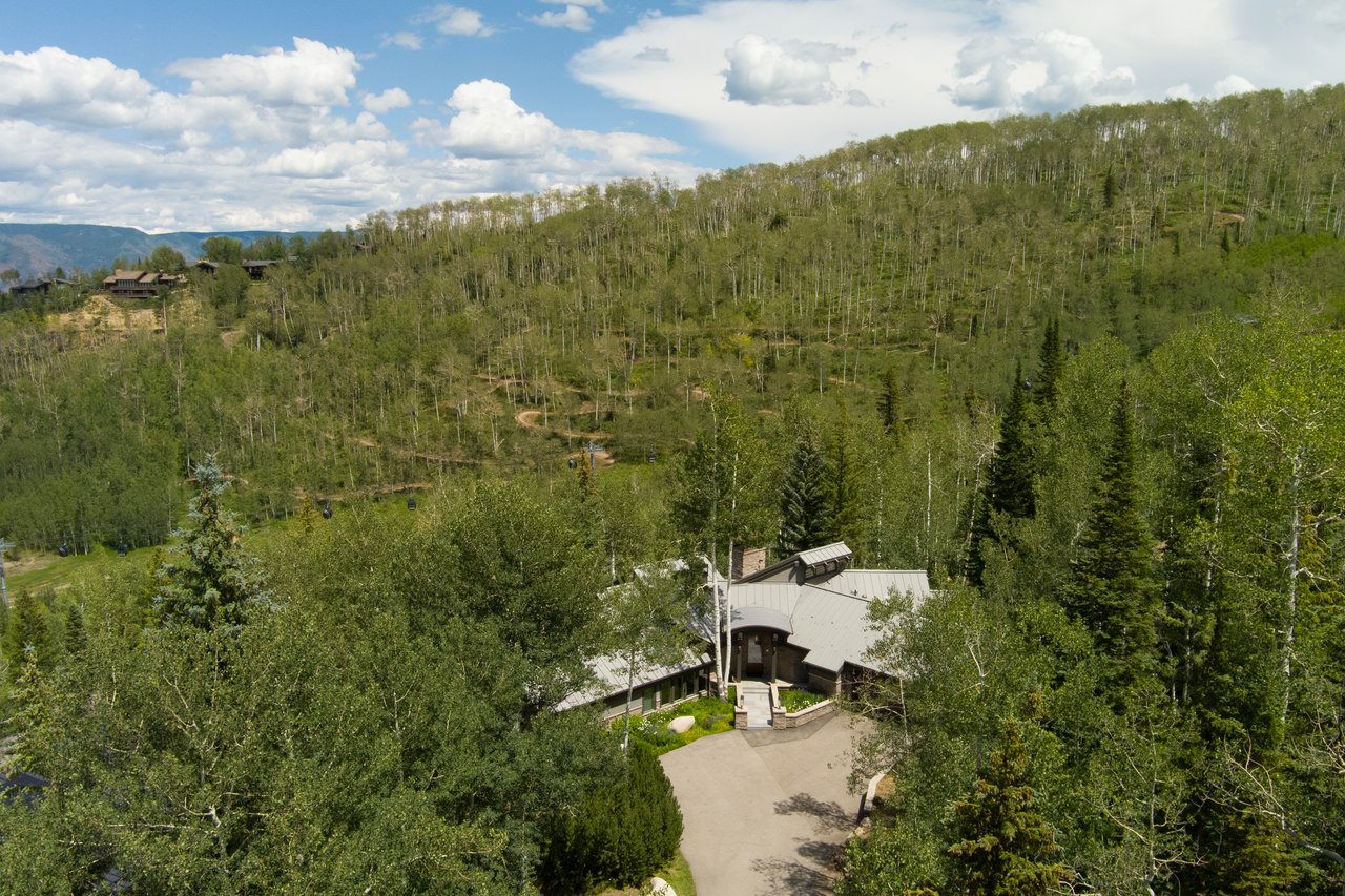 Mountain home among green aspens, with gondola lines crossing the hillside.